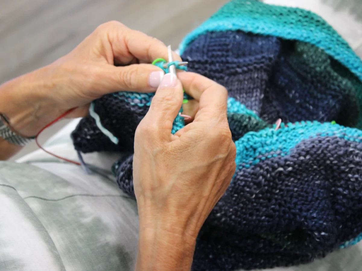 Hands knitting with blue and turquoise yarn